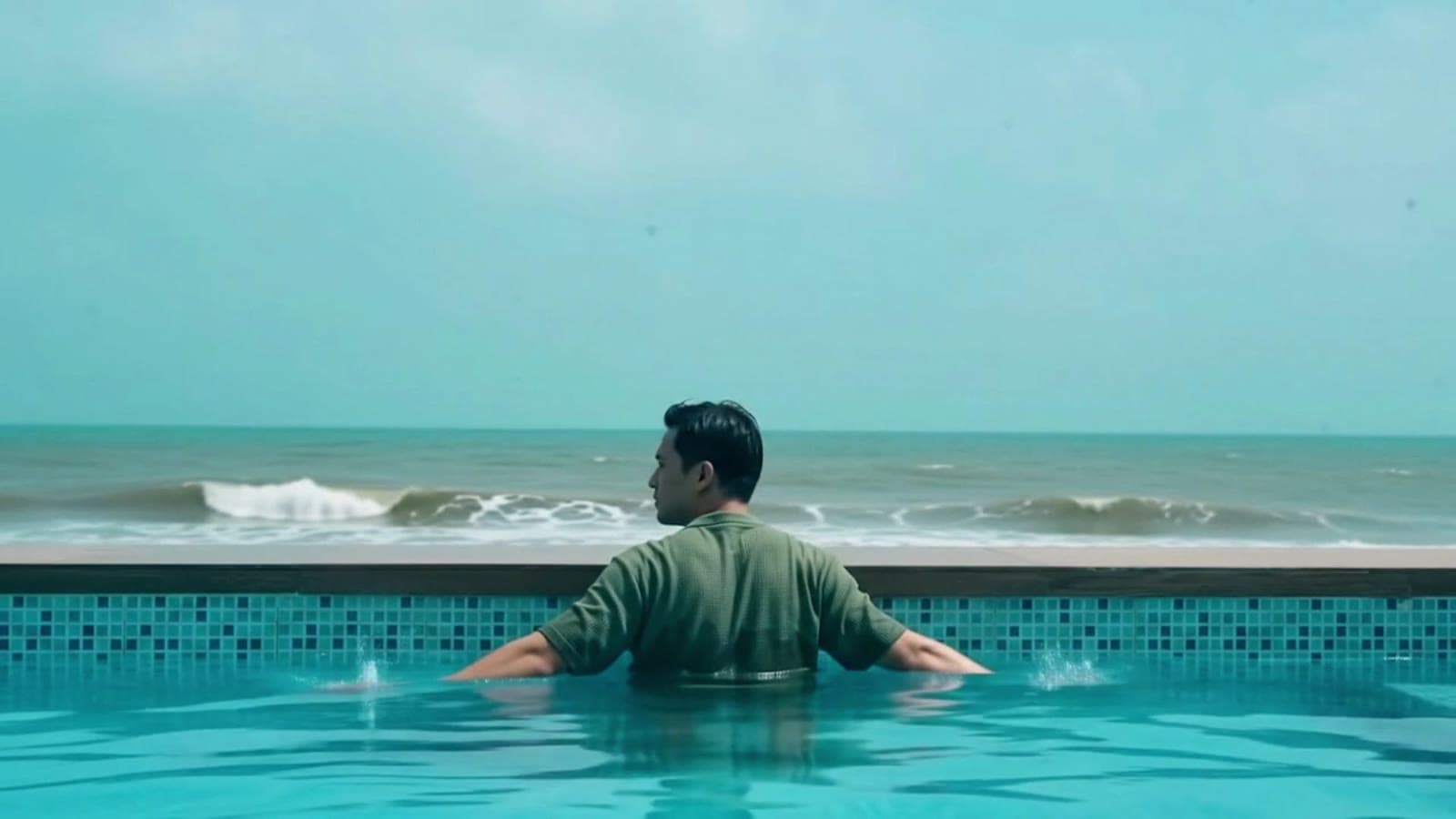 Man standing in an infinity pool facing the ocean
